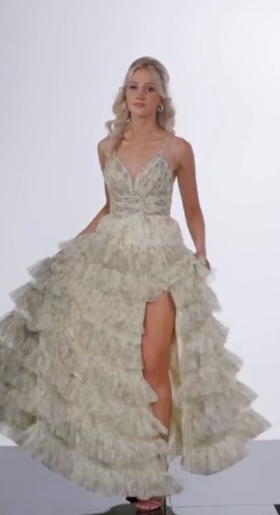 The Jovani 36571 is a vision of elegance in the formal collection. Crafted from mesh, this A-line prom dress showcases a delicate floral print, infusing the gown with a sense of whimsy and charm. The ruffle skirt adds a playful element, creating movement and enhancing the overall romantic aesthetic. A high slit in the skirt introduces an alluring touch, allowing for graceful movement.