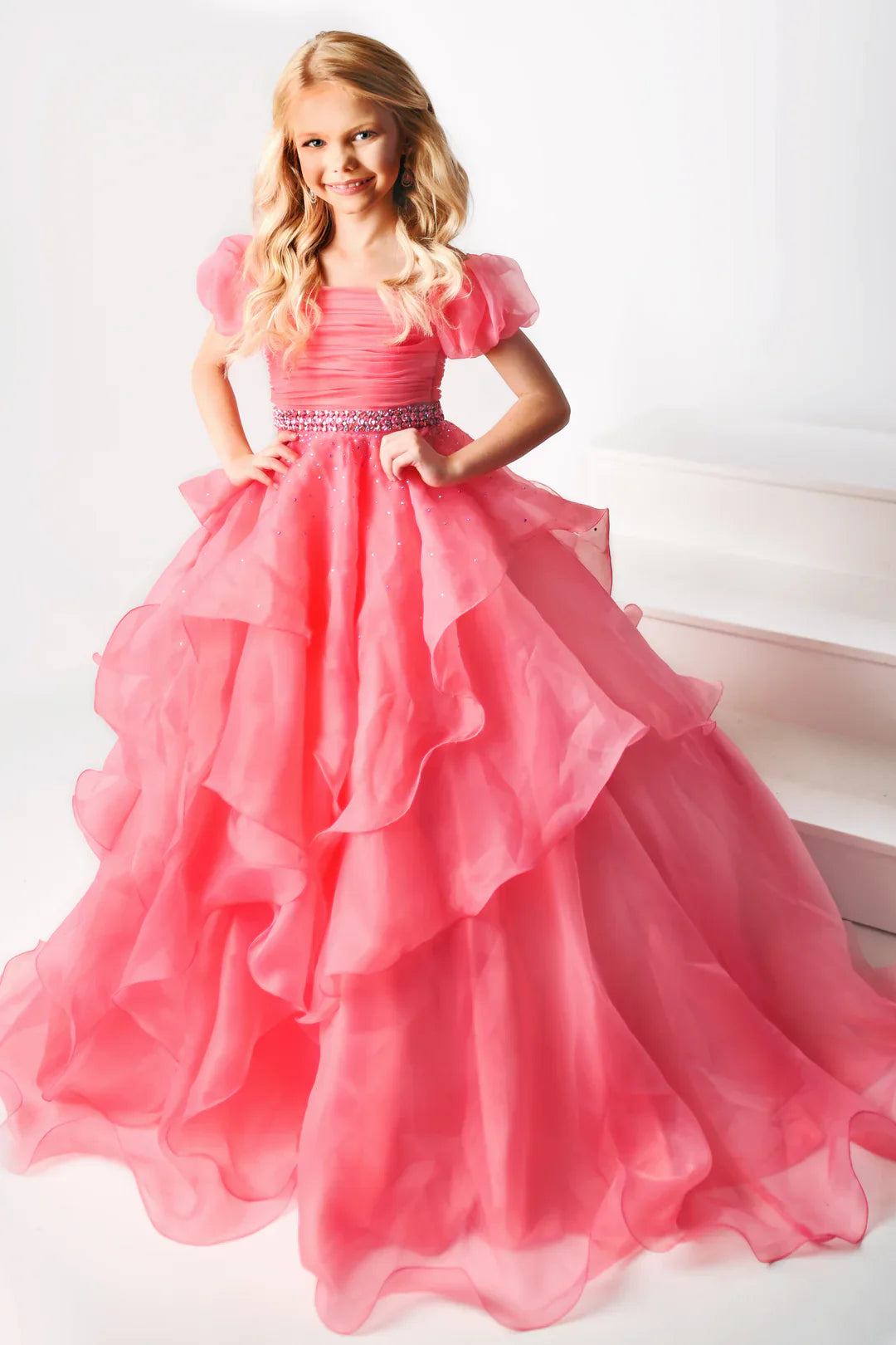 The Ava Presley 38025 Long Ruffle layer A Line Ballgown is designed for girls' pageant wear, offering classic style and sophistication. Its off-the-shoulder design features a puff sleeve, ruffle layer and detailed craftsmanship for an elegant look. Made of soft and durable fabric, it offers superior comfort and long-lasting wear.  Sizes: 2-16  Colors: Light Blue, Coral, White