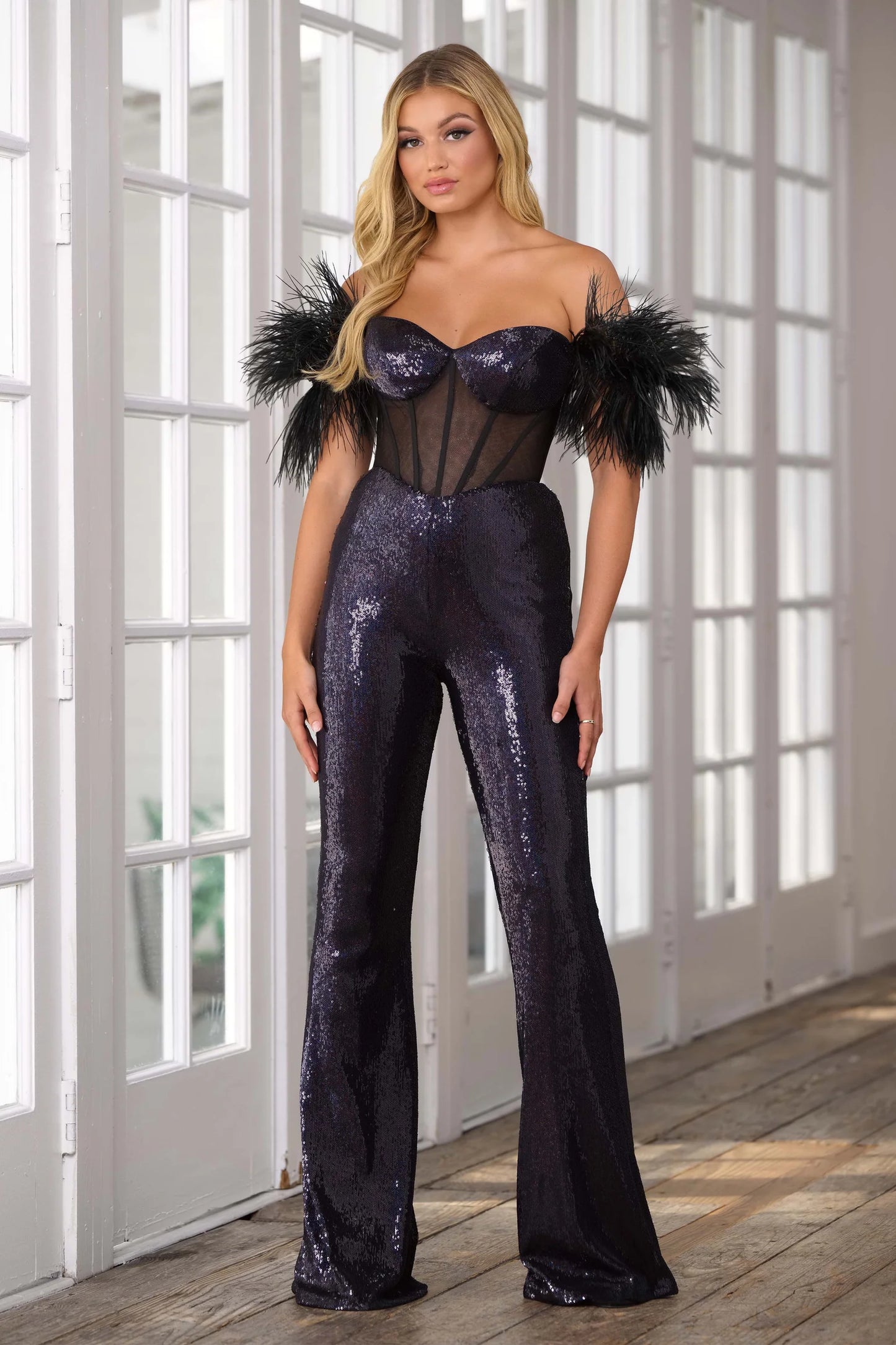 The Ava Presley 39577 Long Sequin Jumpsuit is designed to make you stand out at any formal event. The intricate sequin detailing and sheer corset add an alluring touch, while the feather off-the-shoulder sleeves add a touch of elegance. Perfect for pageants or other formal occasions.  Sizes: 00-16  Colors: Black/AB, Iridescent White, Light Blue