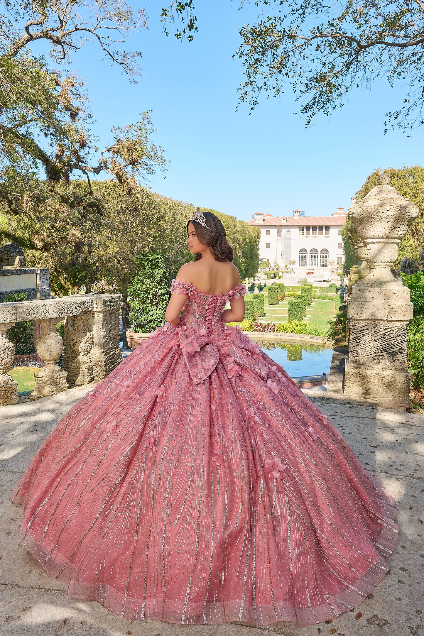 Turn heads and capture hearts in this Amarra 54226 breathtakingly whimsical ball gown! Crafted with exquisite layers of frayed tulle, this full-length dress boasts a feathery, dimensional look that's sure to enchant. The semi-sweetheart neckline paired with charming off-the-shoulder sleeves creates a delicate, feminine frame, accentuated by a fitted waistline that beautifully defines your silhouette. 