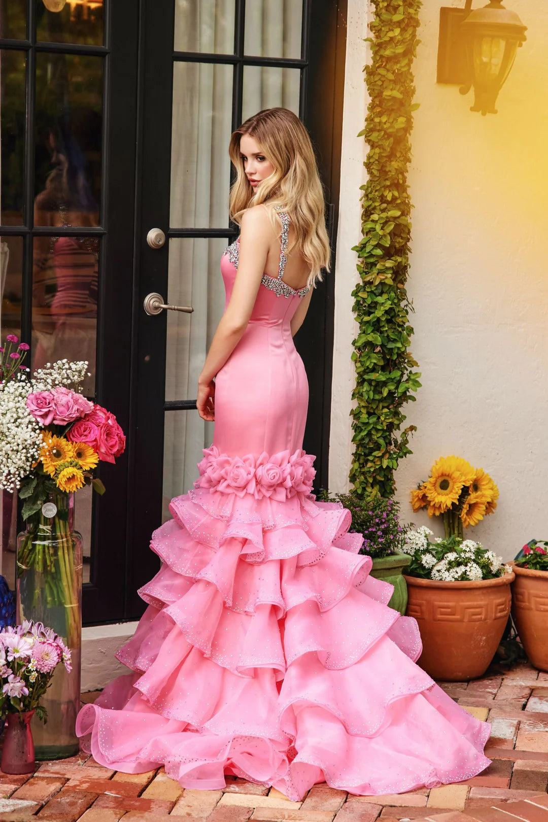 This Ava Presley gown, style 39566, showcases a stunning and elegant look in pure white. The fitted bodice features a sweetheart neckline accented with intricate beaded embellishments along the straps and neckline, adding a touch of sparkle and sophistication.&nbsp;The mermaid silhouette hugs the body before flaring out into a tiered, ruffled skirt. Layers of tulle adorned with subtle crystal details give the skirt volume and a whimsical touch. Delicate floral appliques sit at the transition from bodice to 