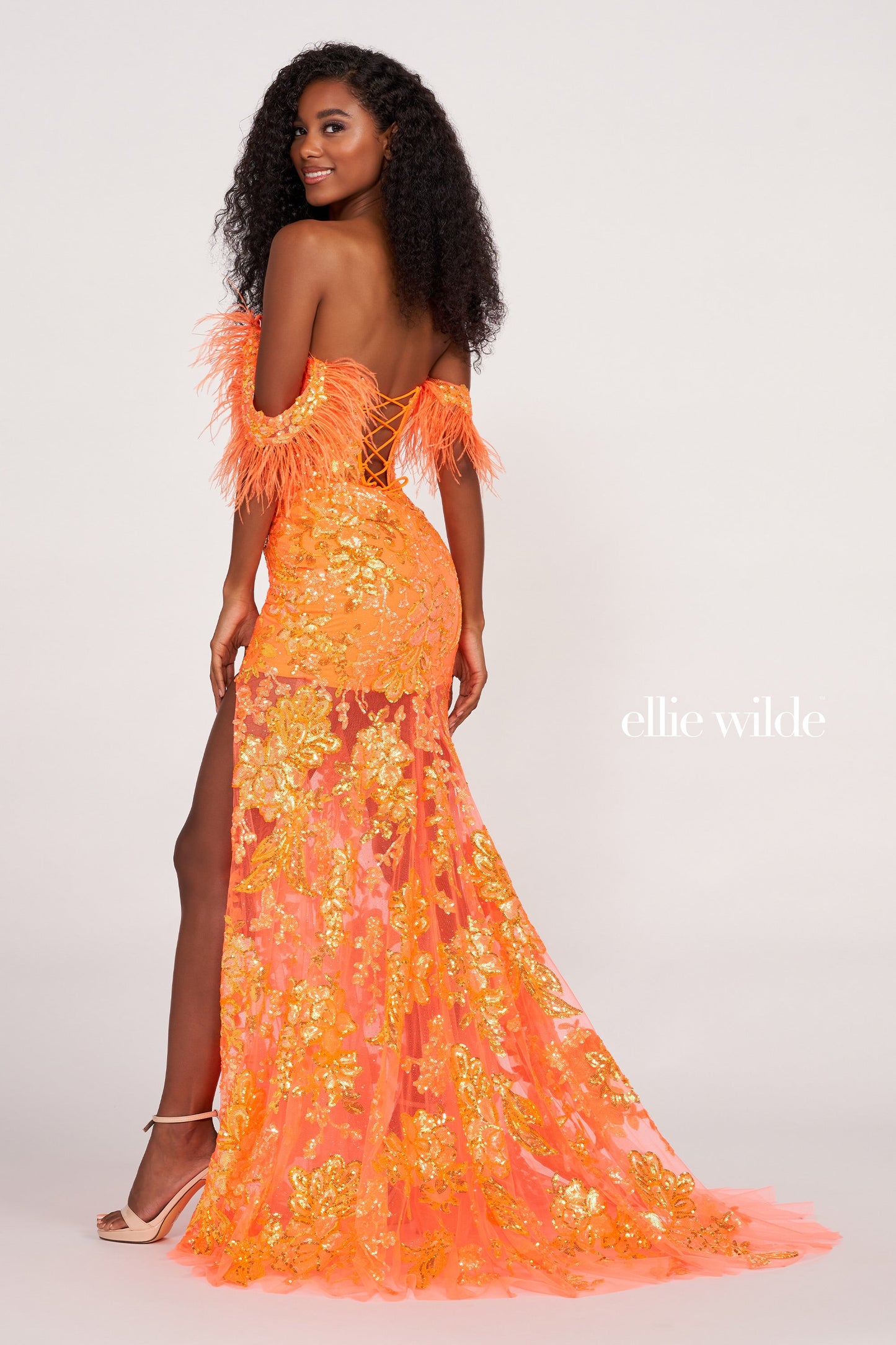 The Ellie Wilde EW34034 is a glamorous formal gown featuring an off-the-shoulder neckline, corset bodice, and a full-length sheer sequin skirt with a side slit. Festooned with a beautiful feather trim, this dress is sure to make a statement.  Sizes: 00-16  Colors: ORANGE, ROYAL BLUE, LILAC, HOT PINK, SAPPHIRE, SKY BLUE, EMERALD, PURPLE RAIN