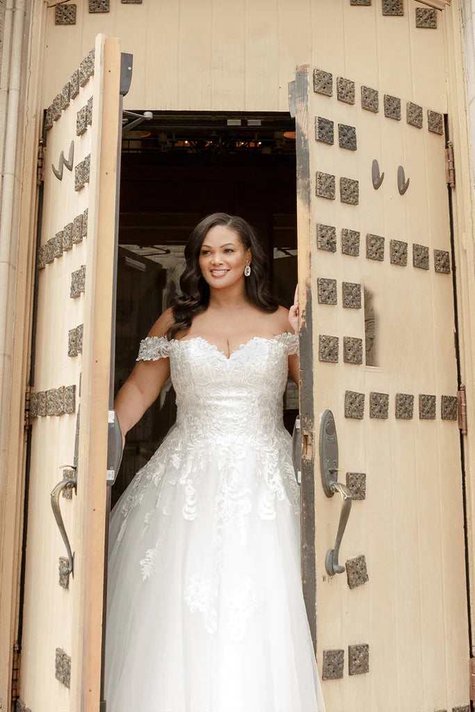 Michelle Bridal For Sydney's Closet MB2310 Soft Bridal Tulle Over Embossed Tulle Floral Pattern Embroidered Lace Appliques Clear Sequins Off The Shoulder Lace Straps  Plus Size "Denali" Bridal Gown. Featuring beautiful lace appliques, clear sequins, and off-the-shoulder straps, the Michelle Bridal For Sydney's Closet MB2310 plus-size wedding dress makes an eye-catching statement. Crafted from embroidered tulle and soft bridal tulle over embossed tulle,