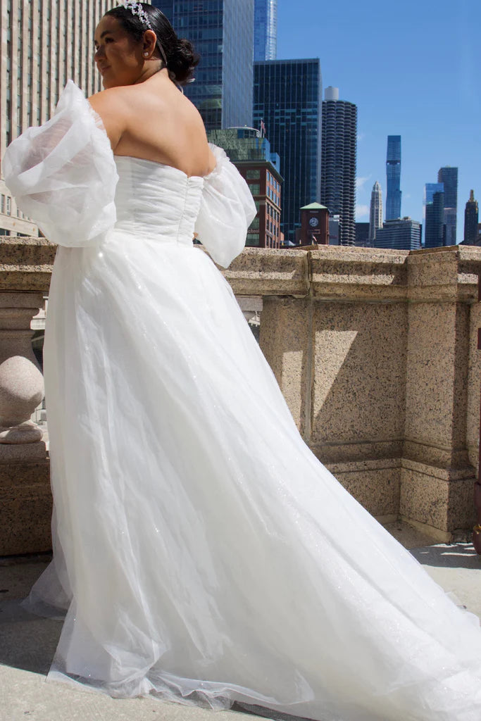 Michelle Bridal For Sydney's Closet MB2324 Ball Gown Silhouette Glitter Tulle Pleated Sweetheart Bodice Sleeveless Strapless Optional Pouf Sleeves Plus Size "Georgina" Bridal Gown. The Michelle Bridal MB2324 "Georgina" Gown features an elegant ball gown silhouette with shimmering glitter tulle and a pleated sweetheart bodice. This plus size dress includes sleeveless straps or optional pouf sleeves for a sophisticated look. Perfect for any special occasion.