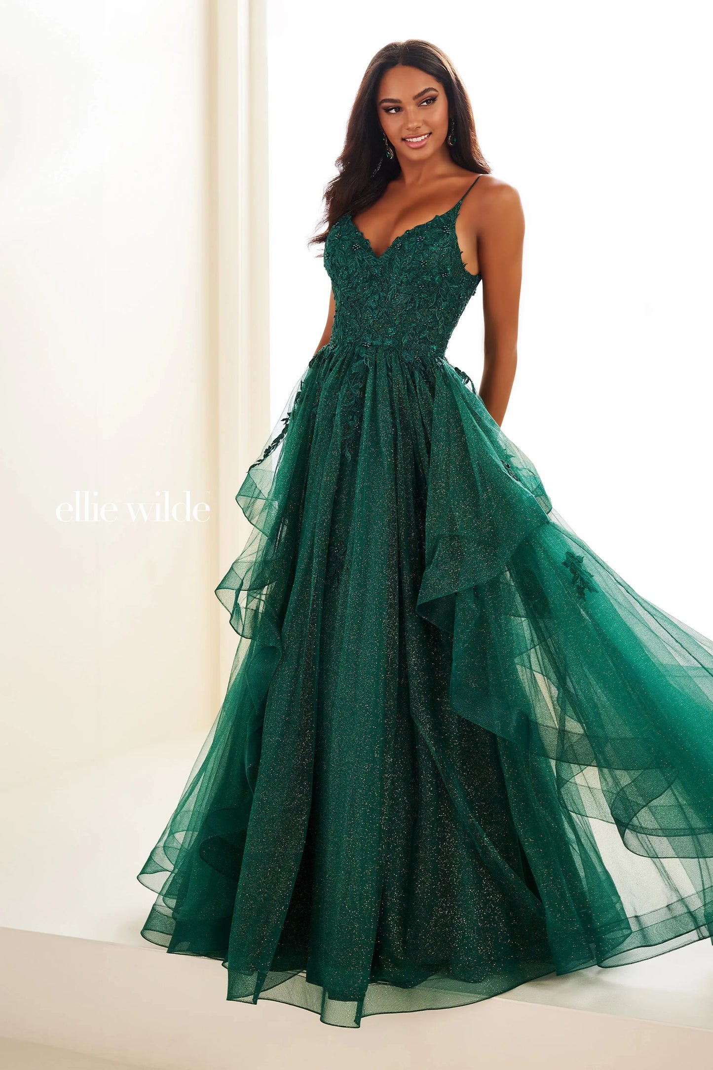 This Ellie Wilde EW3685 dress features sheer lace and a shimmering design for a glamorous look. The A-line silhouette flatters all body types, while the ruffle detailing adds a touch of elegance. Perfect for prom, formal events, and pageants.