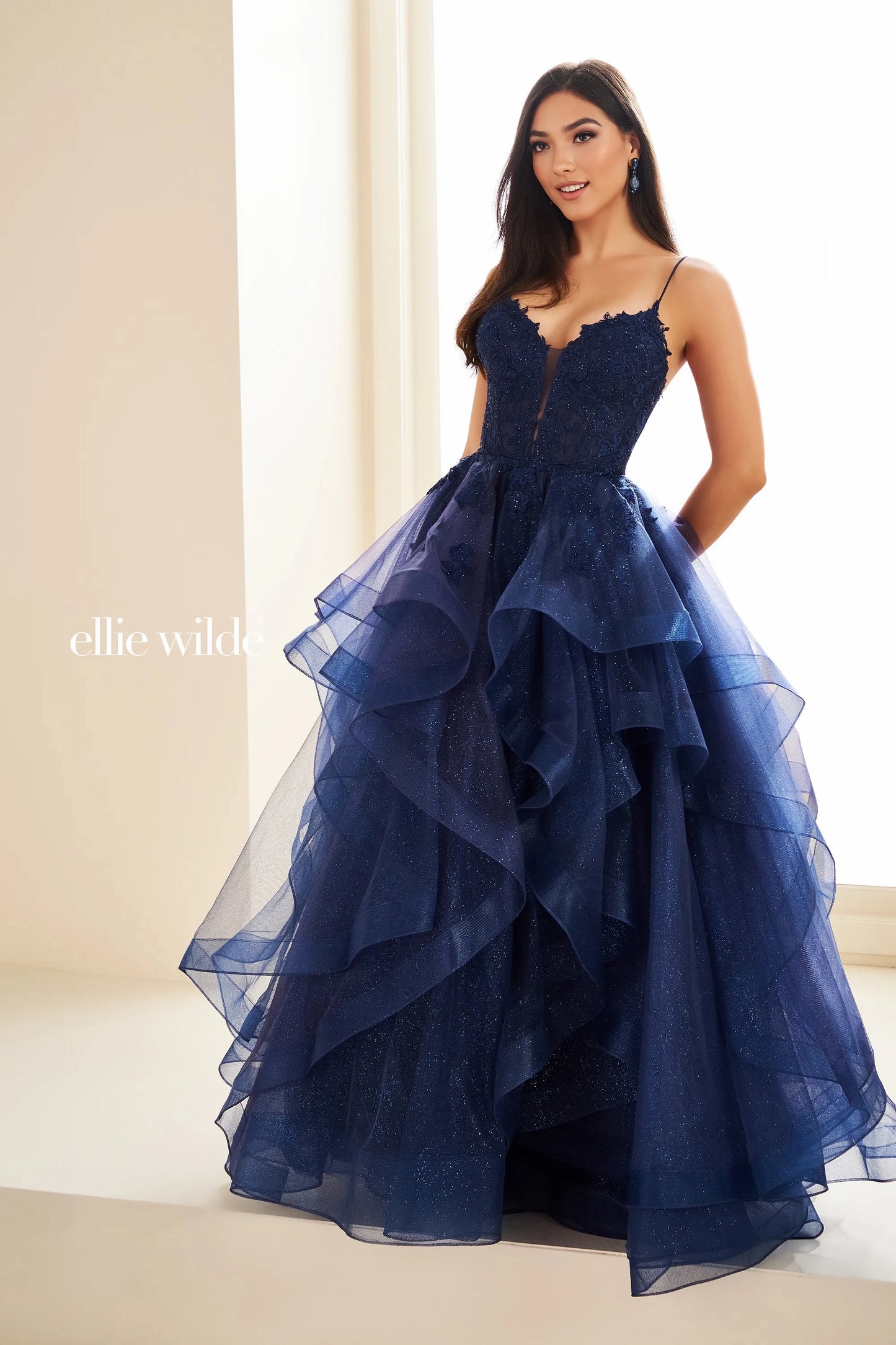 This Ellie Wilde EW36203 prom dress dazzles with a sheer lace corset bodice, ruffle A-line skirt, and shimmering fabric. Create an elegant silhouette with the figure-flattering corset and add a touch of romance with the feminine ruffle detailing. Perfect for a formal evening event, this dress is sure to turn heads.