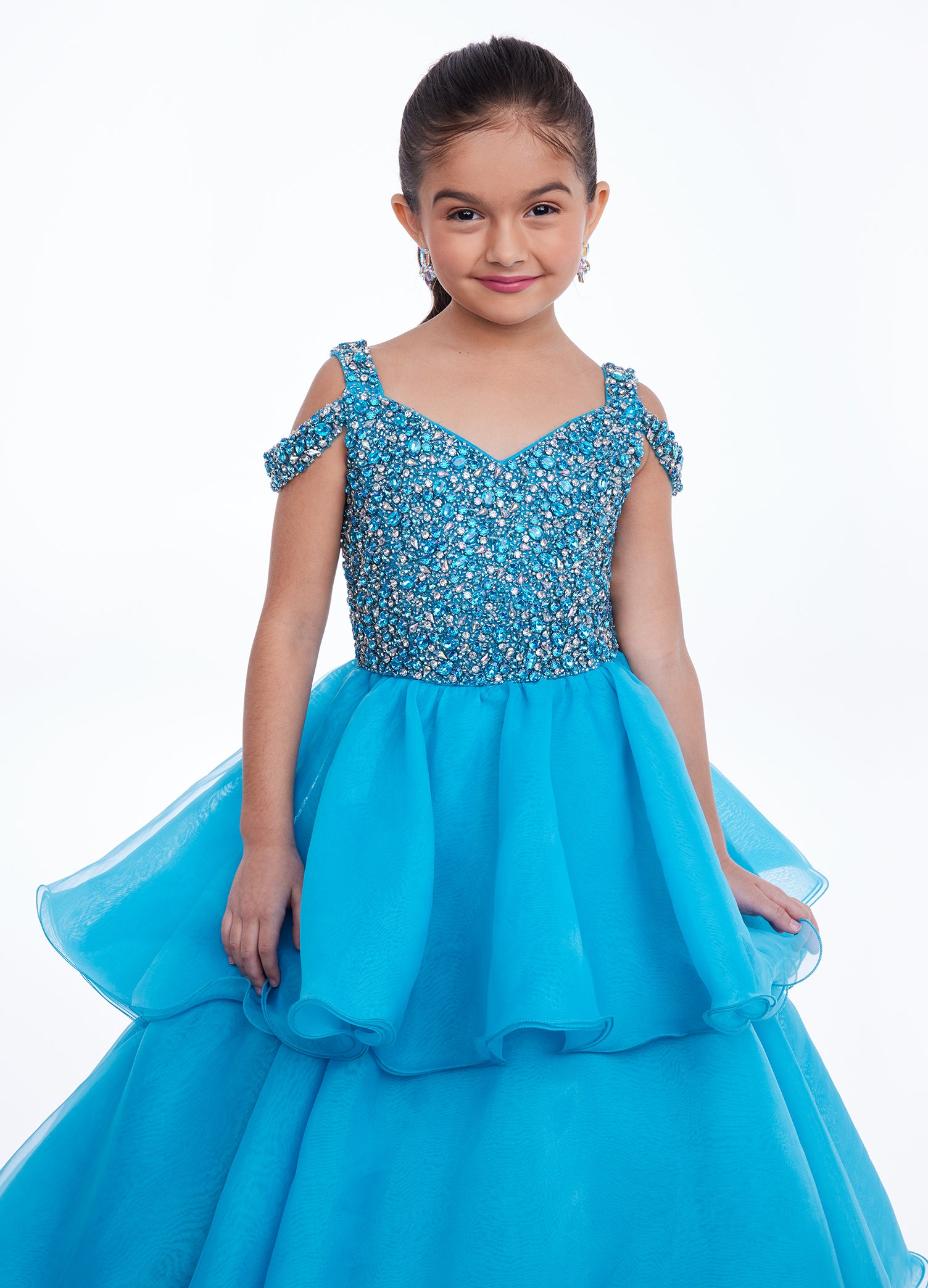 Ashley Lauren Kids 8101 Girls Pageant Dress.  The crystal encrusted bodice on this kids Pageant Gown consists of a slight V-Neckline and off the shoulder straps. The A Line multi-tiered organza ruffle skirt completes the look with a long train.   Available colors:  Hot Pink, Lilac, Turquoise