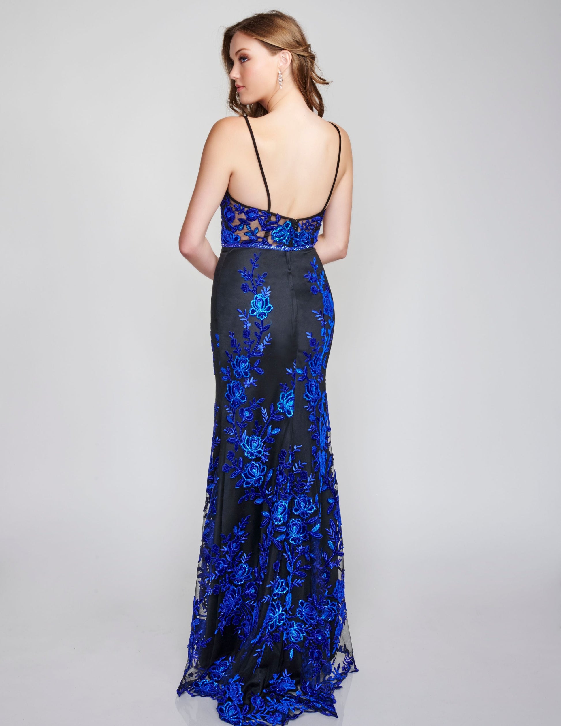 Nina Canacci 2240 Black Royal Long Prom Dress Evening Gown Fit and Flare Floral Lace Dress.  This dress is black with royal blue applique lace through out the dress.  It has a v neckline with sheer panel and a sheer lace back.  The long skirt is a fit and flare style. 